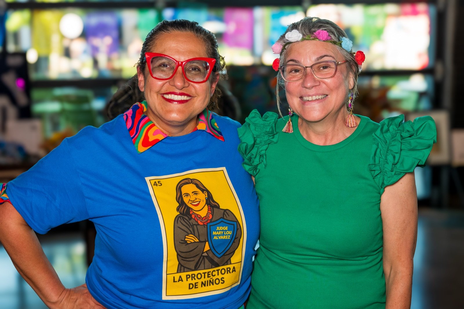 Two friends, one wearing a La Protectora de Niños lotería shirt